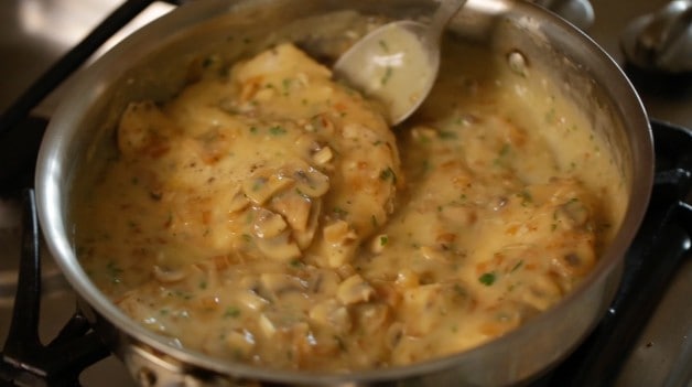 spooning white wine sauce over chicken breasts in skillet