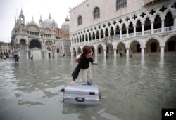 A tourist pushes her floating suitcase in a flooded St. Mark