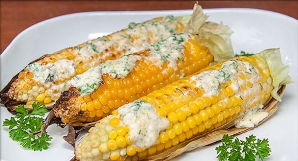 Приготовленная на мангале кукуруза в листьях со сливочным соусом на тарелке