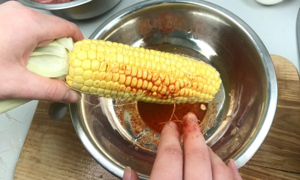 Натирание кукурузного початка смесью растопленного сливочного масла и молотого красного перца