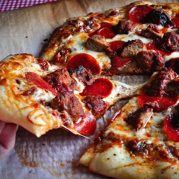 Someone taking a slice of pizza made with homemade pizza dough, pepperoni and sausage.