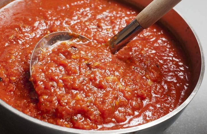 A close up of the tomato sauce being spooned out of a large pot.