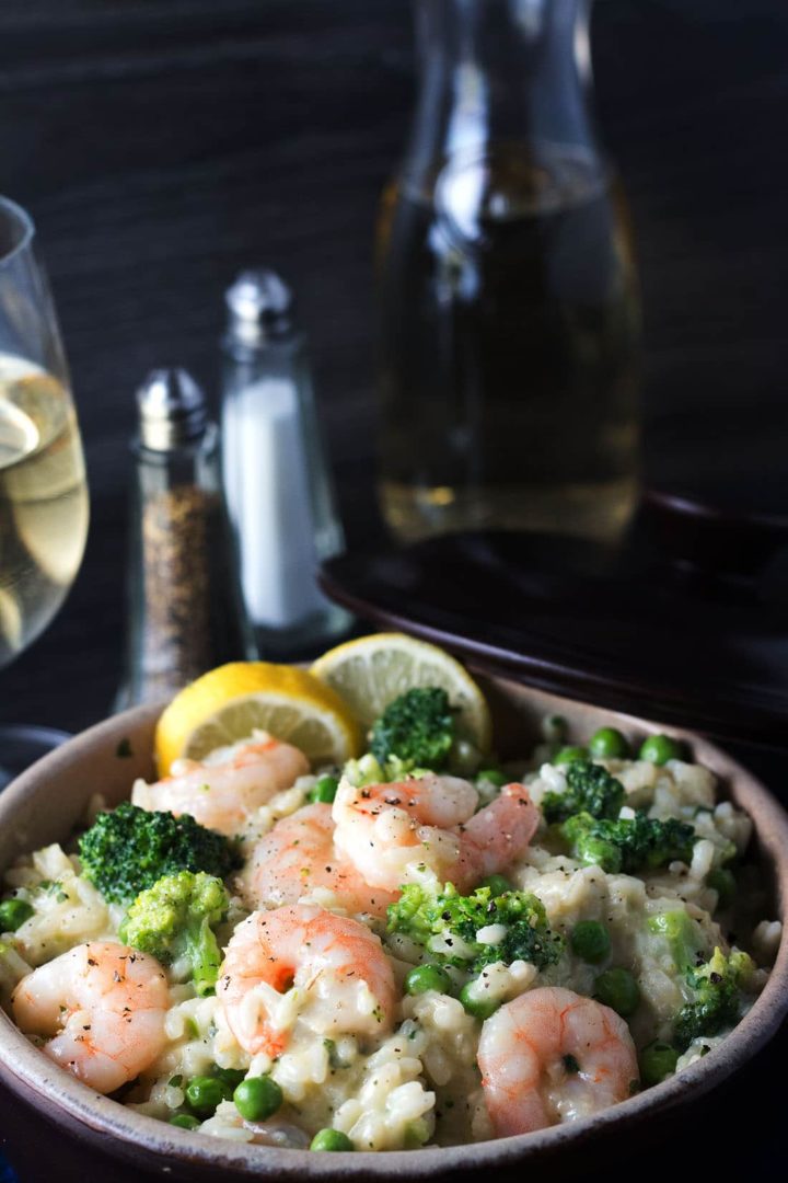 Easy Lemon Shrimp Risotto in a bowl with lemon wedges, a glass of white wine and salt and pepper mills in the background