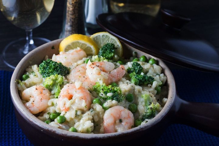 Easy Lemon Shrimp Risotto in a bowl with a glass of white wine and salt and pepper mills in the background