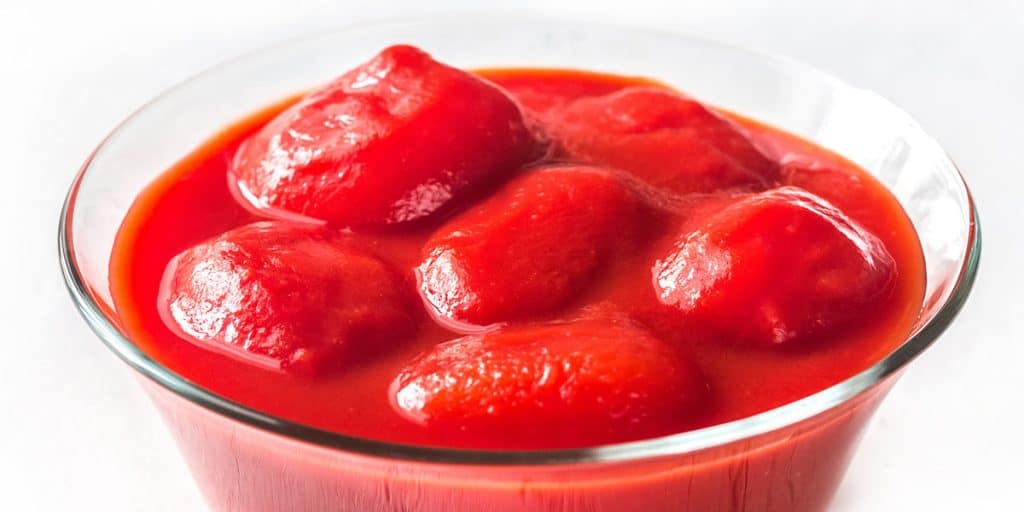 a glass bowl with whole tomatoes in their juice