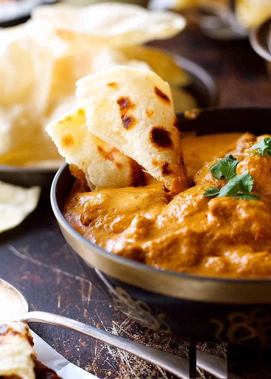 Close up of naan being used to scoop up Butter Chicken