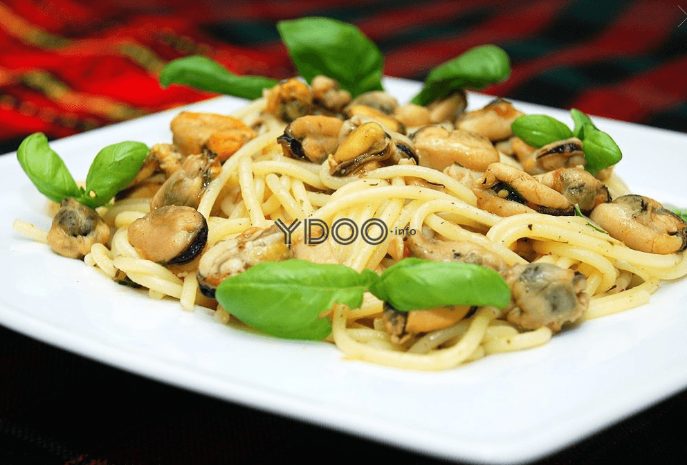 тарелка со спагетти, мидиями и свежими листьямизеленого базилика