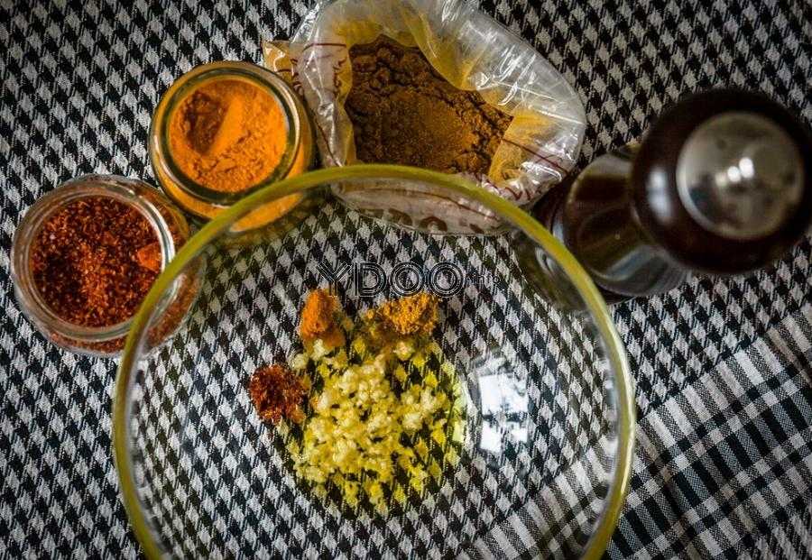 оливковое масло с чесноком, паприкой, куркумой, зирой и молотым черным перцем в прозрачной стеклянной тарелке на столе, рядом баночки и пакетик со специями